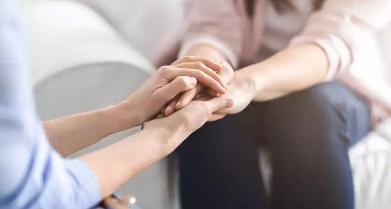 One woman holding the hands of another to comfort her.